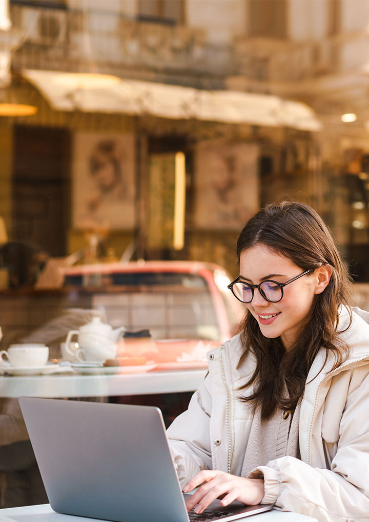 Junge Frau sitzt bei einem Café und tippt in ihrem Laptop